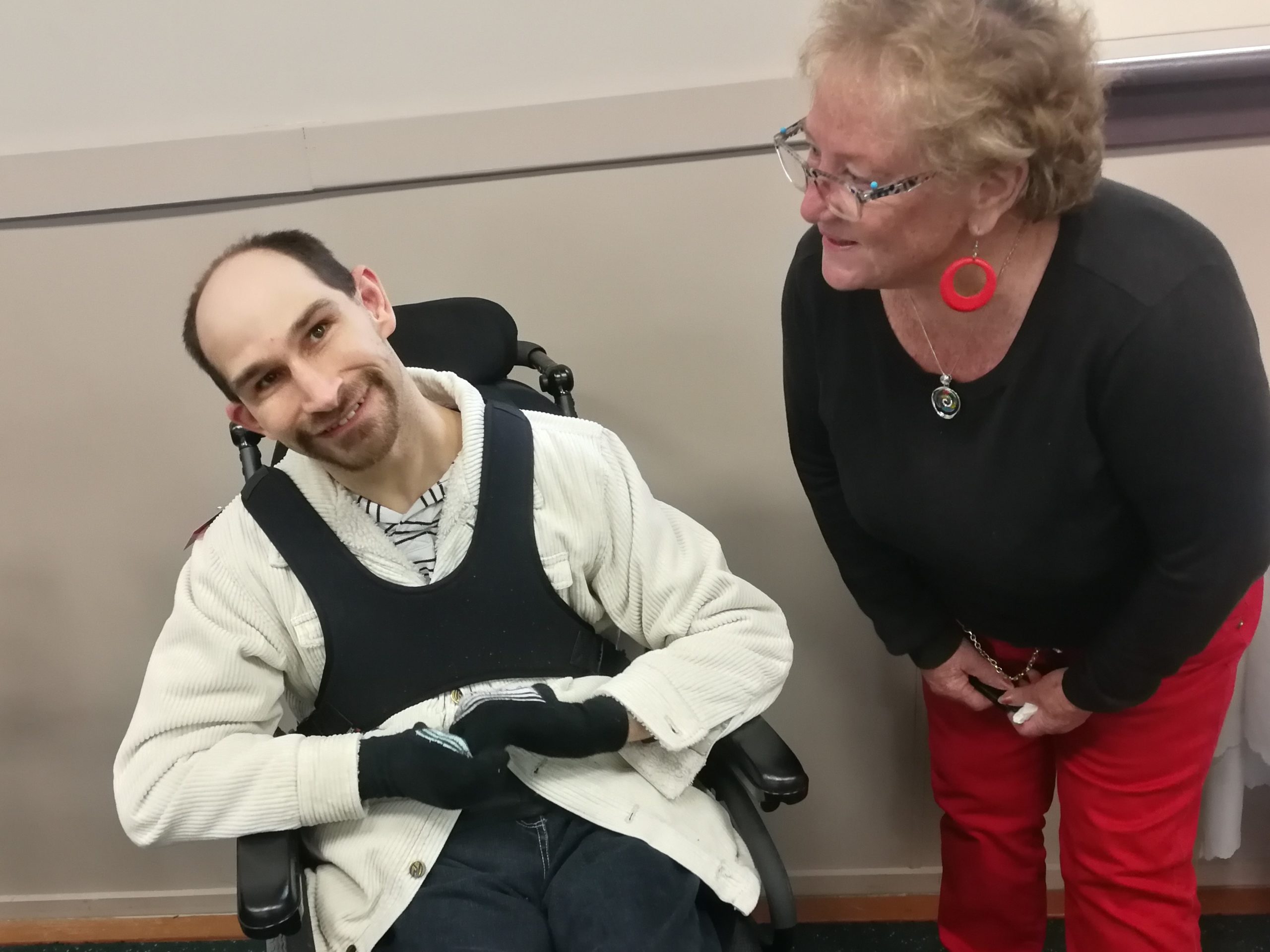 A man in a wheelchair and a woman in a black top, talking and smiling at each other