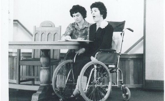 A black and white photo of a young Di and Margie sitting side by side on a stage