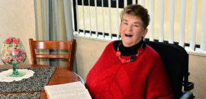 Margie Willers wearing a bright red knitted top sitting at her dining table smiling