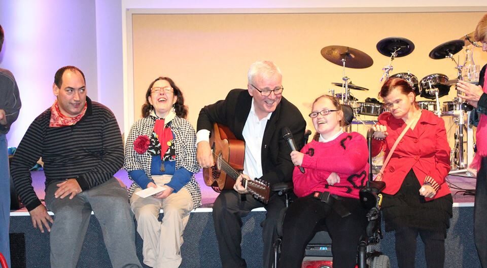 Singer Chris Skinner playing a guitar and singing with people with different physical disabilities