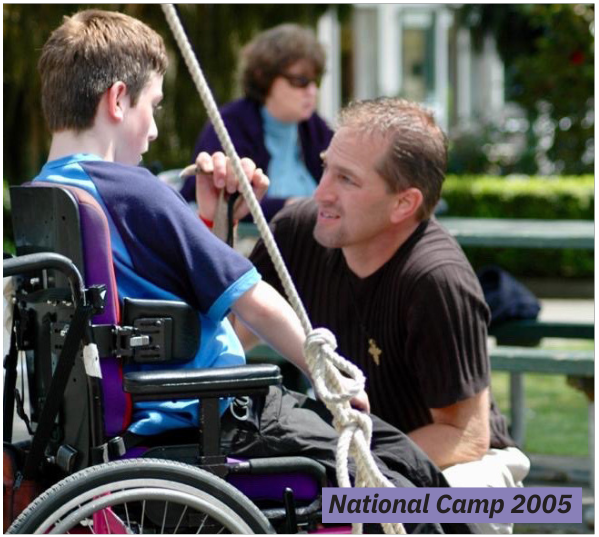 Jack kneeling down talking to a young camper in a wheelchair