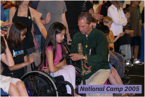 Jack kneeling down, praying with a young female camper with a microphone on stage