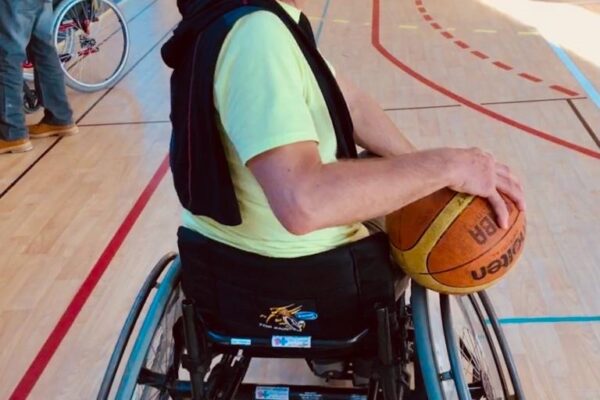 Ps Jack O. smiling at the camera in his wheelchair holding a basketball on a basketball court