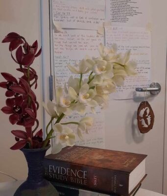 A photo of orchids in a vase in front of some study bibles and some handwritten notes on the wall