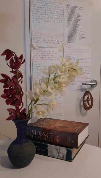 A photo of orchids in a vase in front of some study bibles and some handwritten notes on the wall