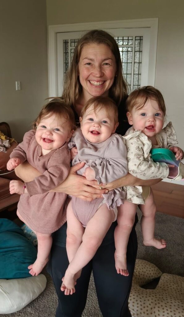 Anna hugging all three triplets at once with their feet dangling off the ground all looking at the camera grinning