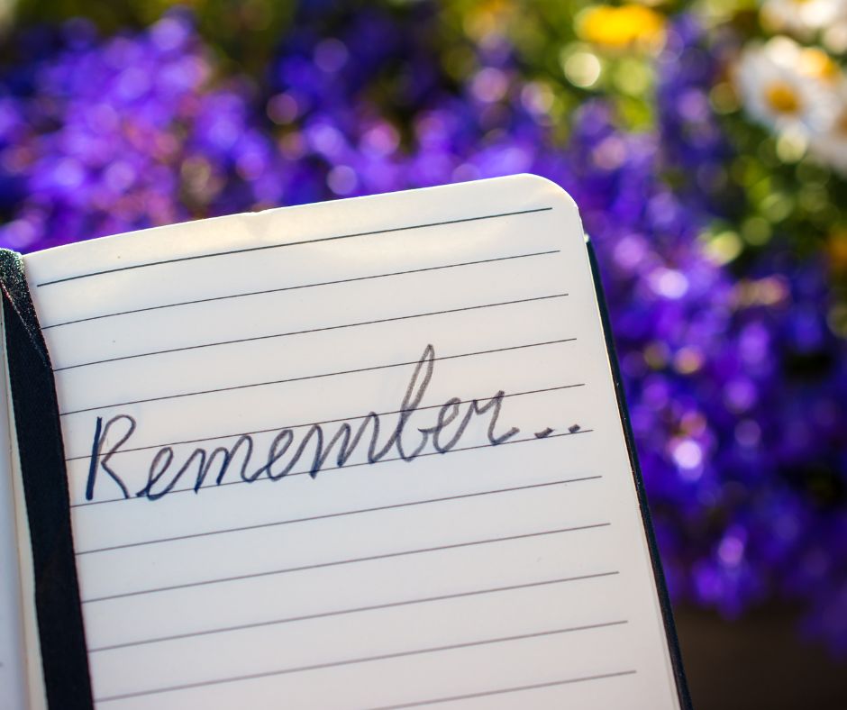 Notebook with the word 'remember...' jotted down with a backdrop of beautiful purple flowers