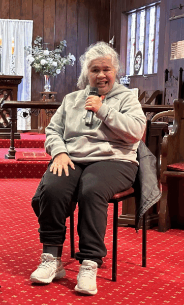 Amanda sits on a chair at the front of a church, smiling as she speaks into a microphone.