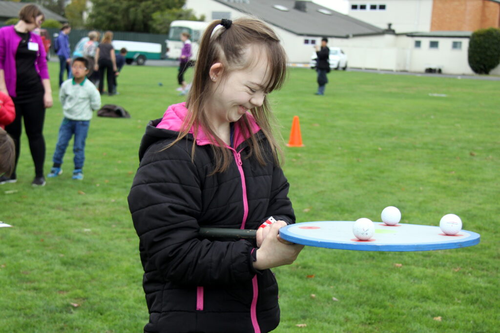 Young woman at an Elevate Camp balancing ping pong balls on a large flat bat