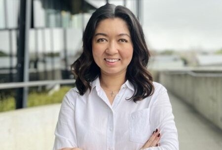 Olivia has black medium length hair and wears a professional white button up shirt.