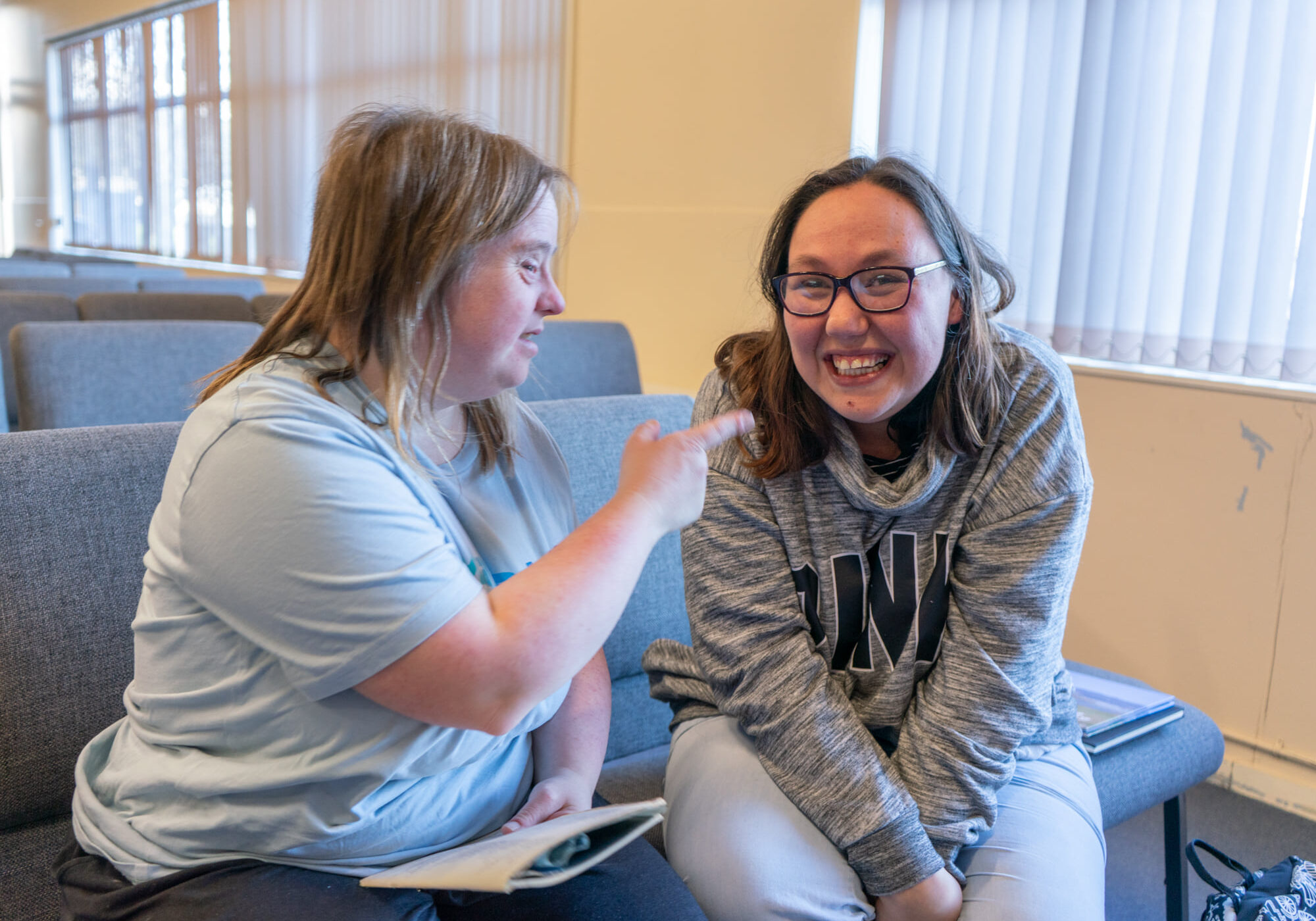 Two young ladies are laughing together on a bench inside