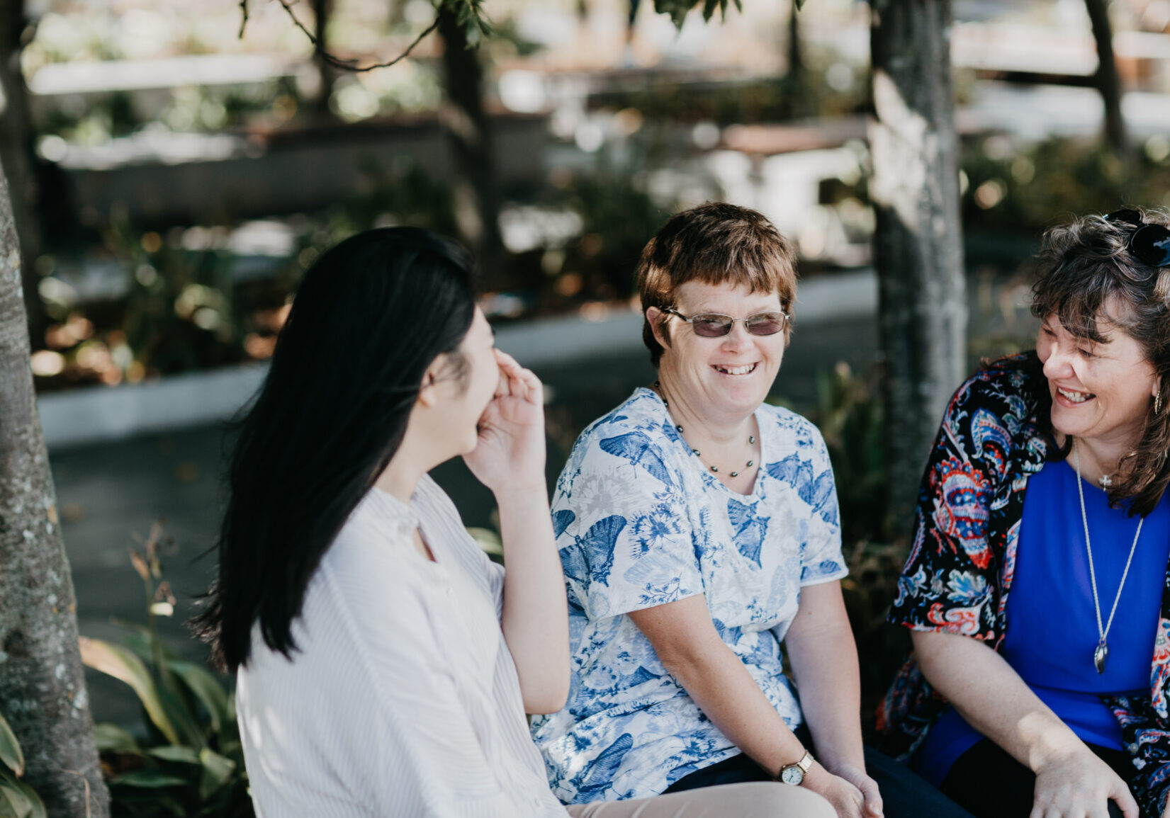 Three ladies sitting, talking and laughing in a park