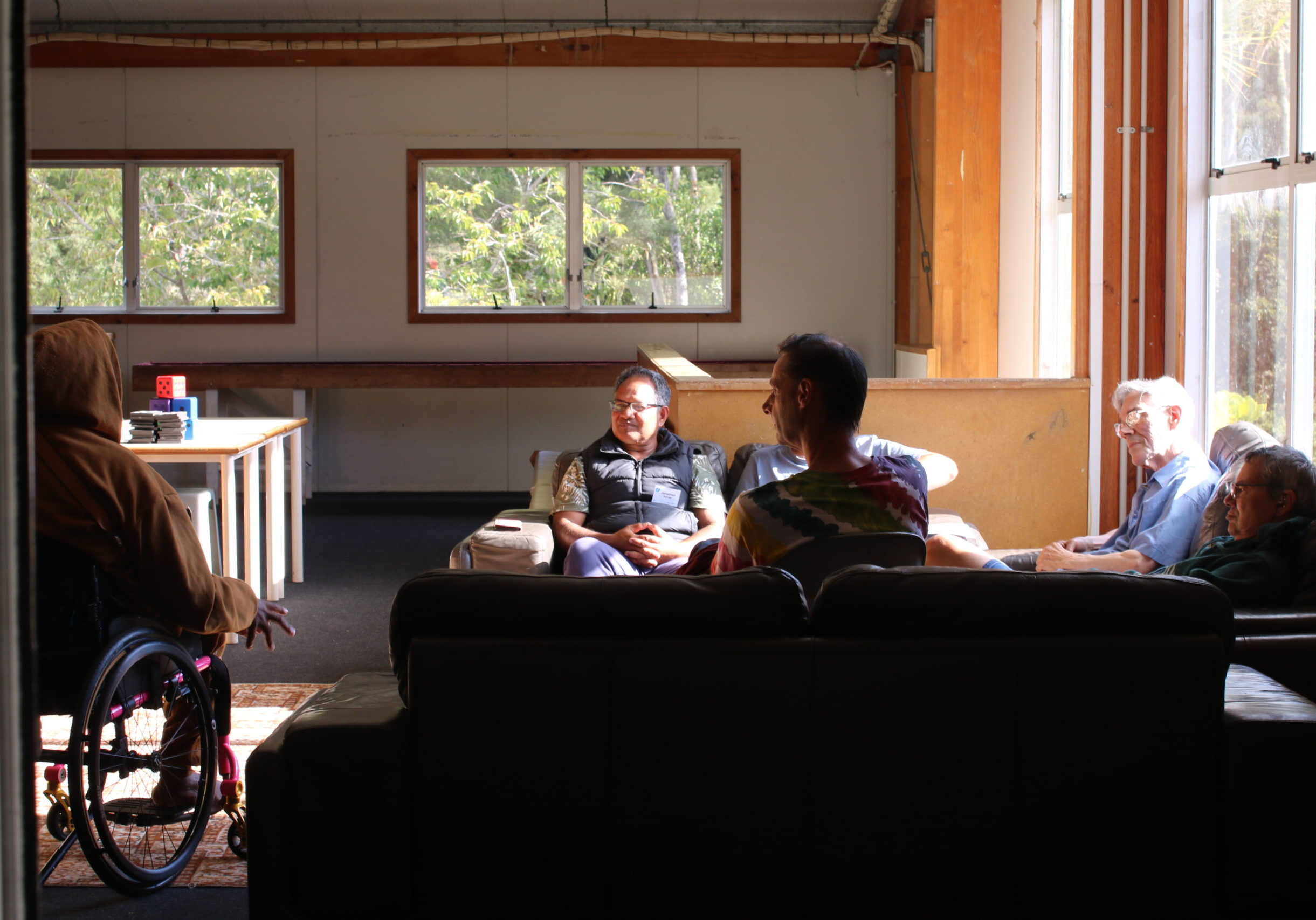 Sunlight is streaming into a living room where people are chatting together in a circle