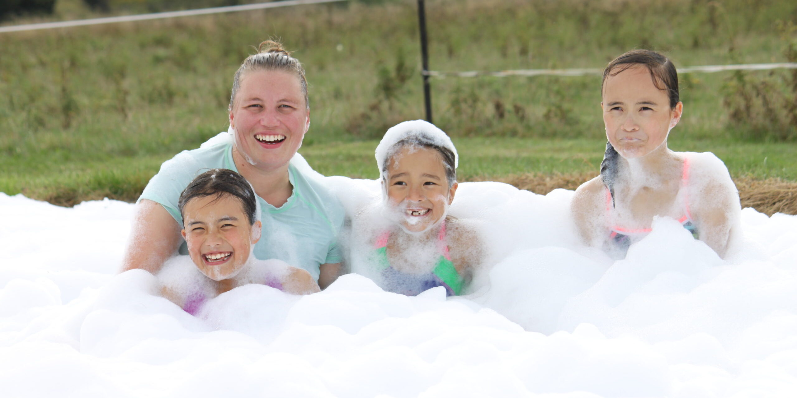 Four people sitting in a large pile of bubbles at the bottom of a waterslide laughing