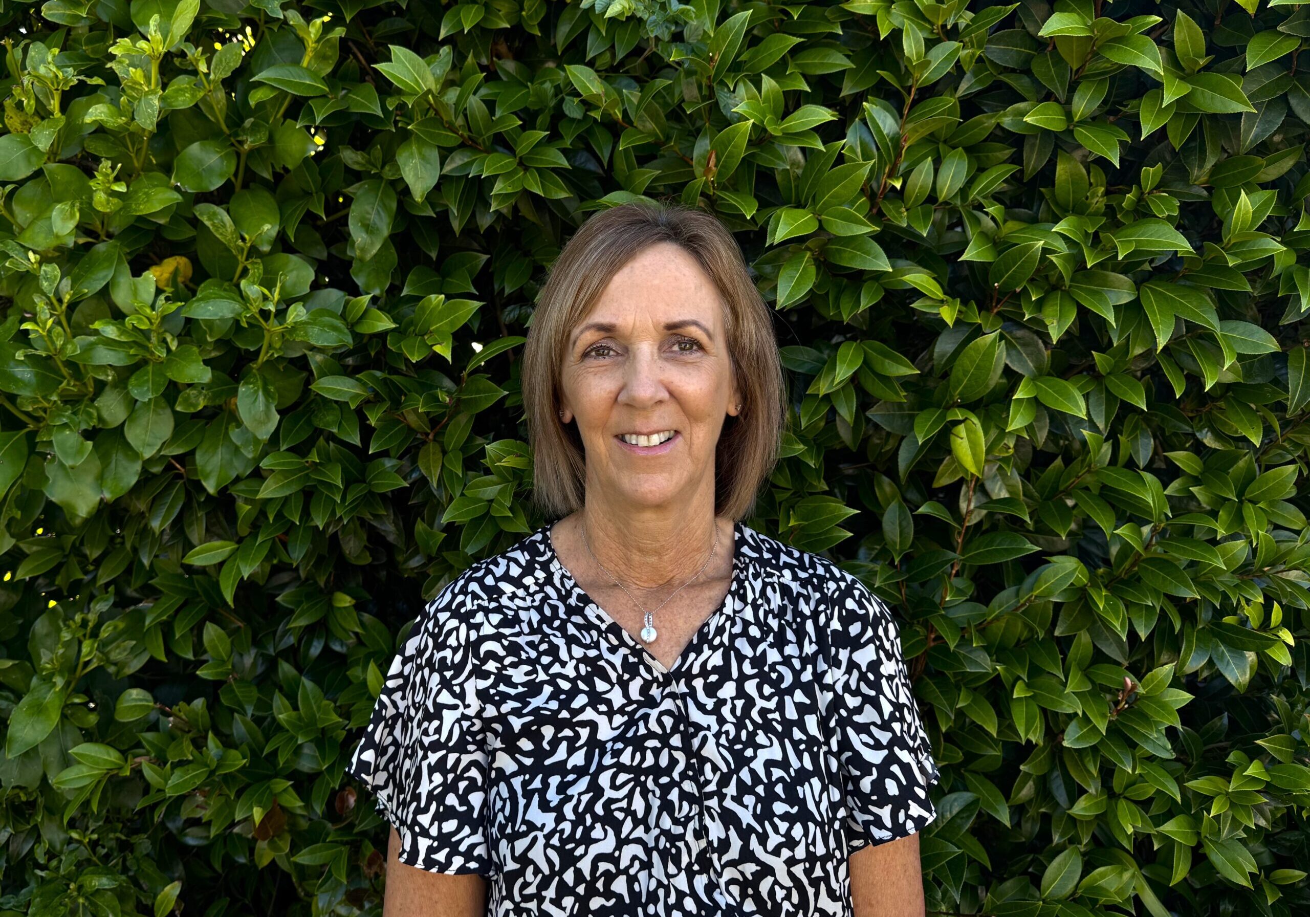 Sarah has short brown hair and wears a smart shirt with a black and white pattern.